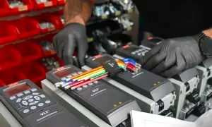 Ręce w czarnych rękawiczkach podłączają kolorowe przewody do falowników VLT AutomationDrive, kluczowych dla sterowania wektorowego.