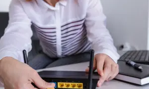 Ręce podłączają kabel do routera, pokazując, jak wejść na router. Obok leży laptop i notatnik.