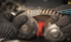 Zużyty pasek klinowy piszczy, jego zęby są postrzępione. Mechanik w rękawicy ogląda uszkodzony element.