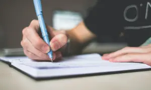 Dłoń pisze niebieskim długopisem w notatniku. Przyszły skrót inżynier tworzy swoje pierwsze notatki.