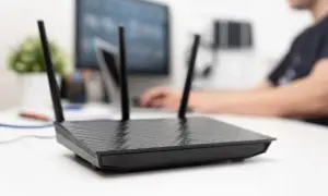 Czarny router z antenkami na biurku, obok monitora. Dowiedz się, jak aktywować kartę SIM w routerze, aby cieszyć się szybkim internetem.