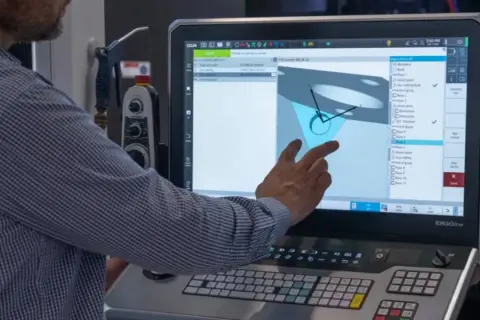 Operator pracuje nad sinumerik programowanie, dotykając ekranu z modelem 3D i listą operacji.