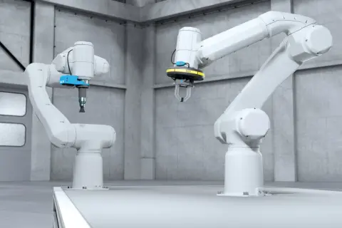 Dwa białe ramiona robotyczne w hali produkcyjnej, jedno z chwytakiem, drugie z przyssawką, gotowe do sterowania robotem.