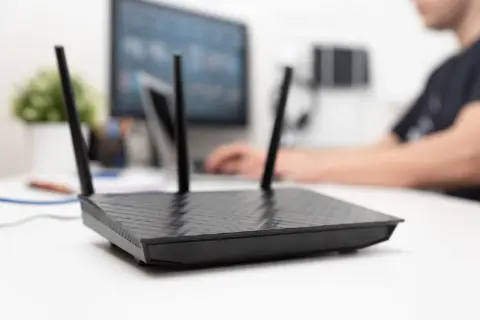 Czarny router z antenkami na biurku, obok monitora. Dowiedz się, jak aktywować kartę SIM w routerze, aby cieszyć się szybkim internetem.