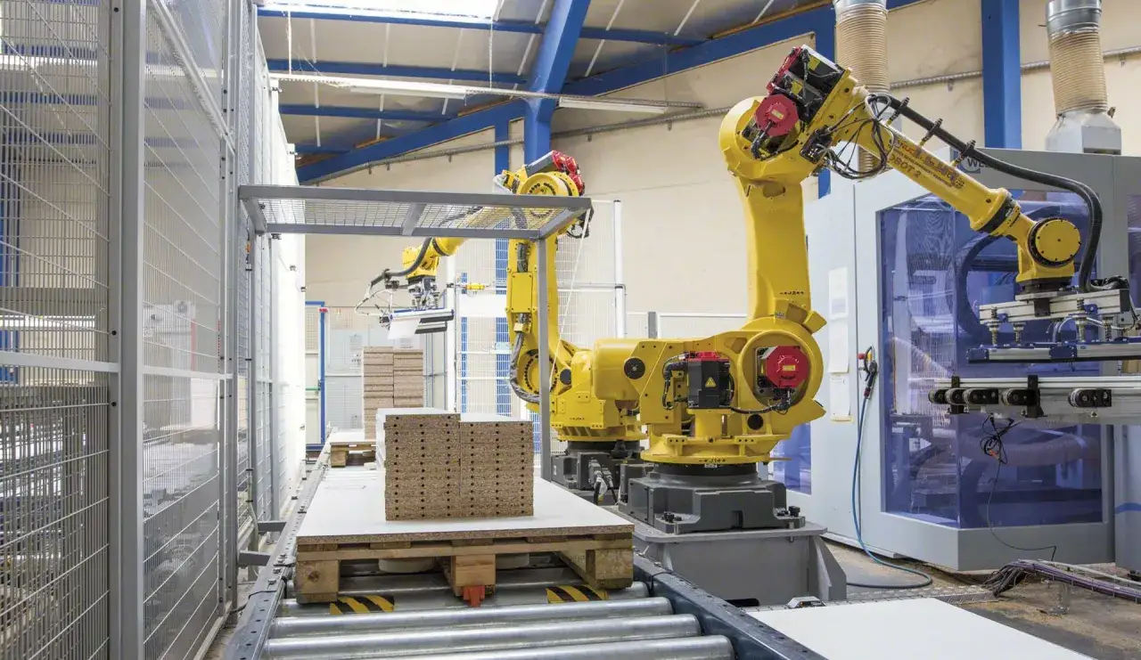 Dwa żółte roboty przegubowe pracują w fabryce, układając paczki na paletach.
