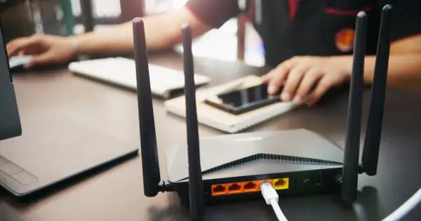 Router co to? Urządzenie z antenkami, podłączone kablem, zapewniające łączność internetową. W tle osoba korzystająca z komputera.