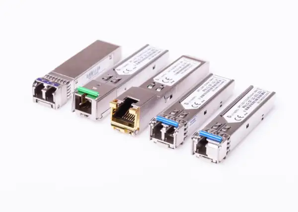 Różne moduły SFP i SFP+ w metalowych obudowach, niektóre z zielonymi lub niebieskimi złączami, inne z pozłacanym portem RJ45.